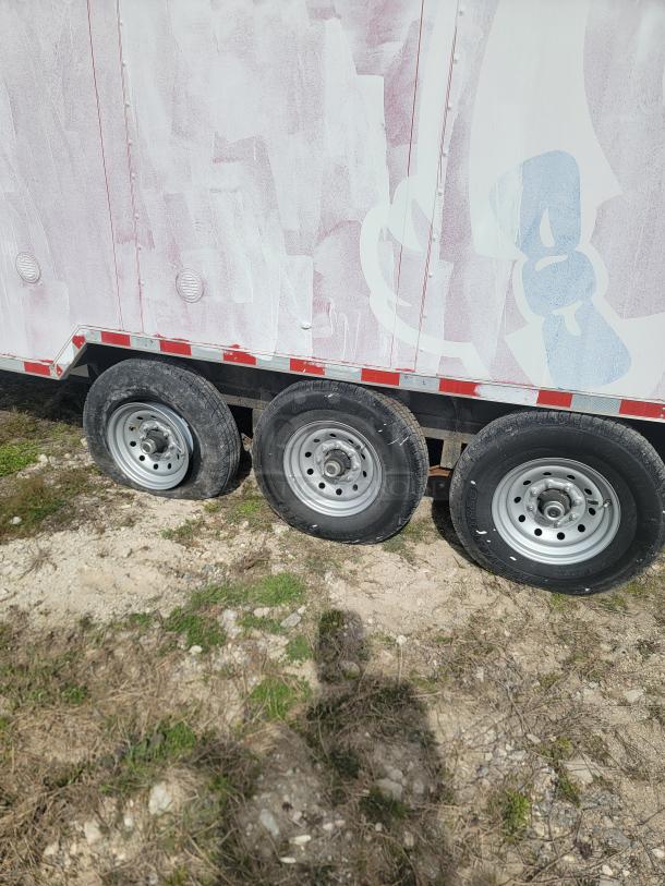 Triple-axle trailer with faded design; visible tires show wear. Trailer exterior has partial pink and blue coloring.