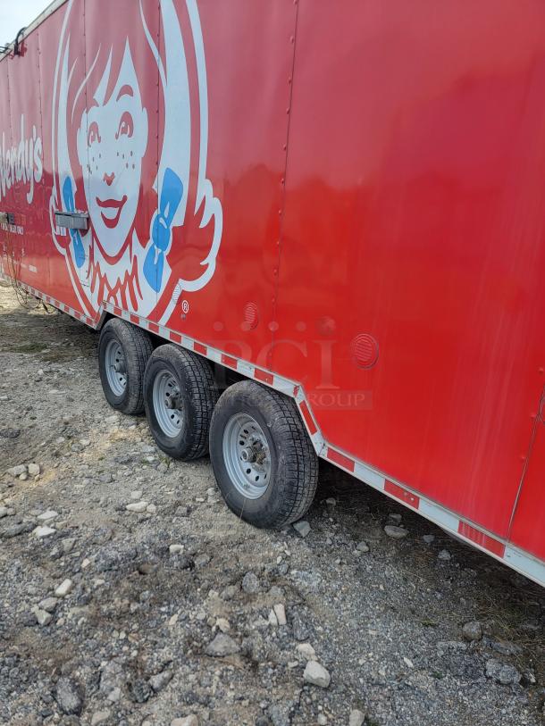 Red Wendy's branded trailer with three wheels, visible dirt and wear, featuring logo of girl with pigtails and blue ribbons.