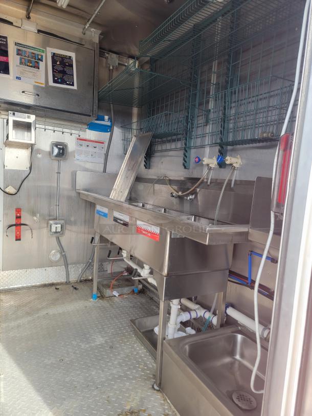 Industrial food truck interior with stainless steel sinks, shelves, and plumbing fixtures. Clean and well-maintained condition.