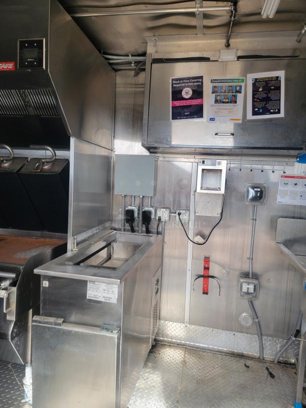 Industrial kitchen setup with stainless steel equipment, ventilation hood, power outlets, and safety signage. Used condition.