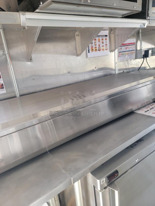 Stainless steel commercial kitchen counter with prep table, storage shelves, and sandwich menu display. Good condition.