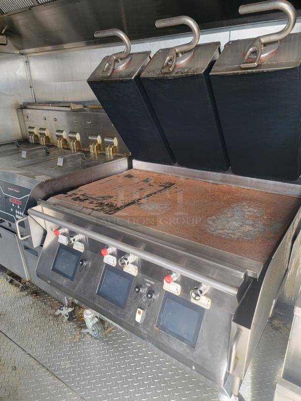 Commercial flat-top griddle with multiple controls, showing signs of surface rust, lids, and digital displays. Stainless steel.