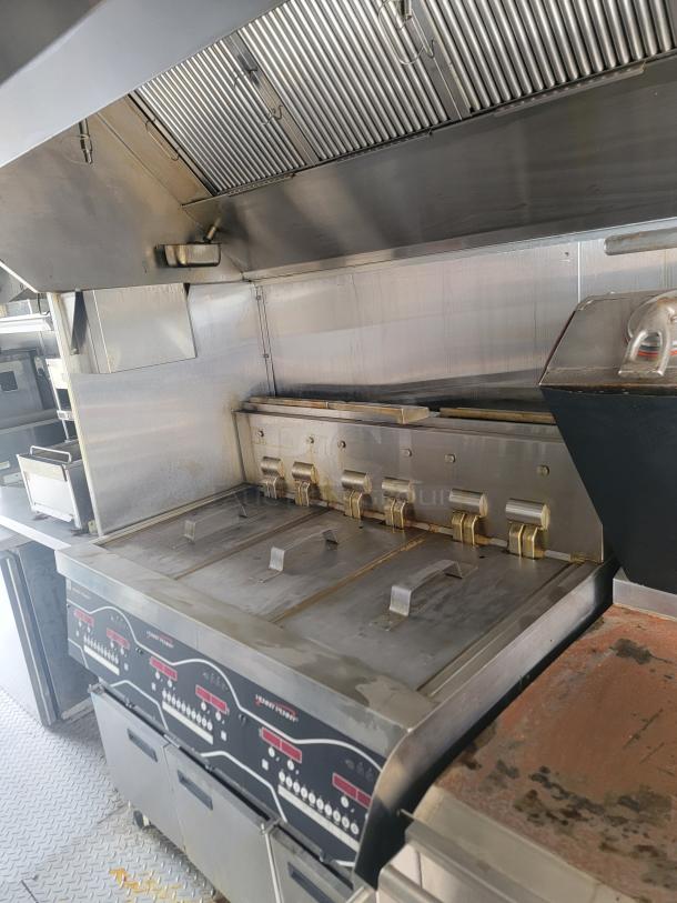 Commercial kitchen equipment with multiple stainless steel fryers, hood ventilation, and control panels, used condition.