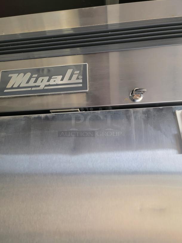 Migali stainless steel refrigeration unit, features brand logo and vent. Slight surface wear, indicating used condition.