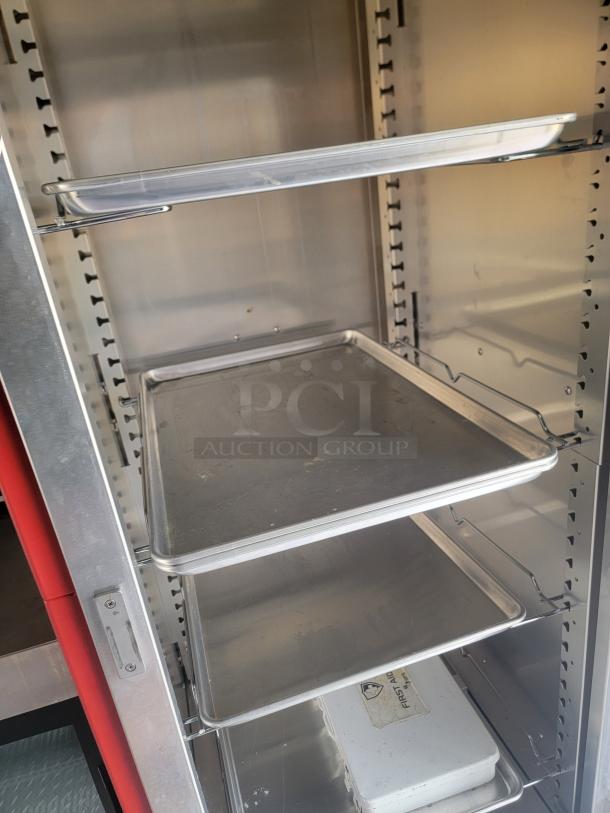 Stainless steel food warming cabinet with adjustable shelves, in good condition, showing a latching mechanism and interior trays.
