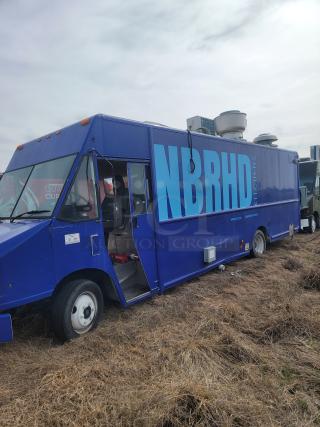 Blue food truck labeled "NBRHD Kitchens," parked on grass, open side door, equipped with kitchen ventilation units.
