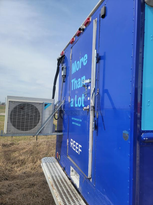 Blue mobile unit with "More Than a Lot" and "REEF" branding. Features rear door, handles, and Daikin air conditioning unit.