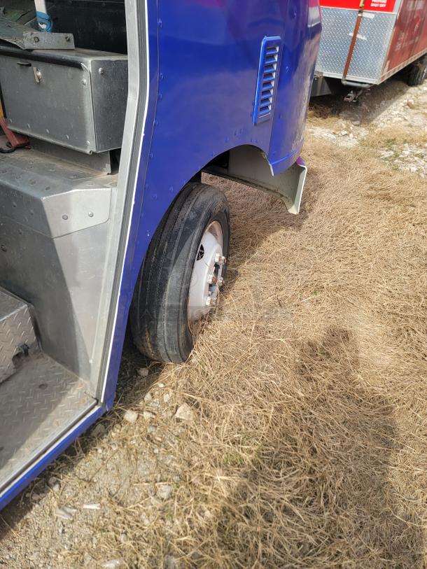Close-up of a vehicle's rear wheel and part of the body. Visible metallic steps and paneling indicate utility features. Overall, the condition appears used.