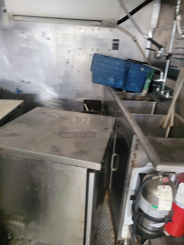 Industrial kitchen equipment with stainless steel surfaces, a blue storage crate, and fire extinguisher. Signs of use visible.