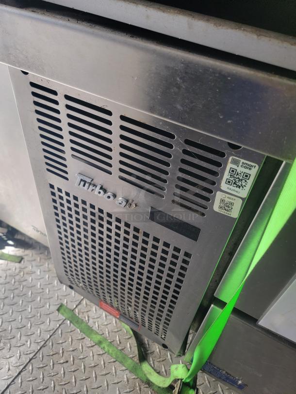 Commercial grade refrigerator unit with Turbo Air branding, showing metal vented panel. Labels include QR codes for maintenance info. Good condition.