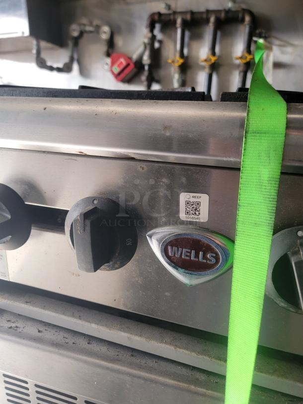 Wells stainless steel cooking appliance with control knobs. Features brand logo. Slight surface wear. QR label visible.