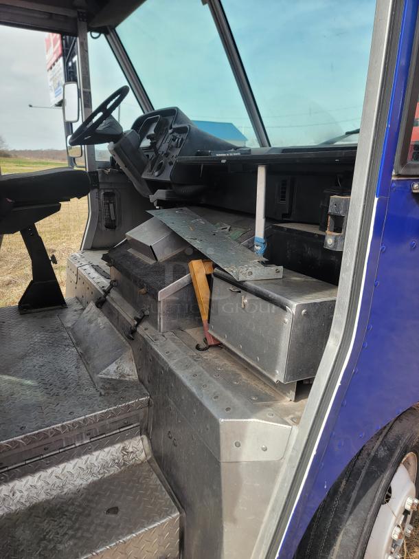 Interior of commercial delivery truck cab, showing a worn dashboard, steering wheel, metal steps, and a storage compartment.
