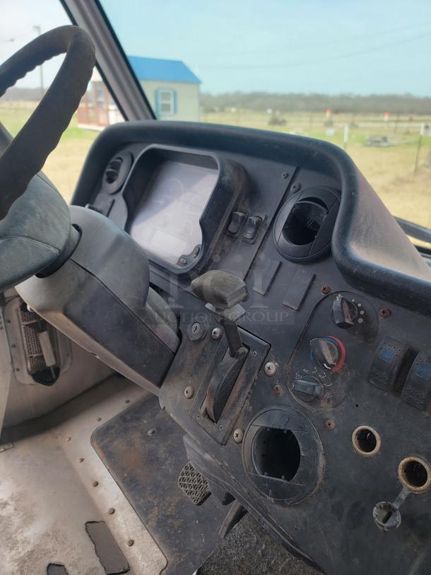 Dashboard of a vintage vehicle with a worn steering wheel, manual controls, and faded gauges in used condition.