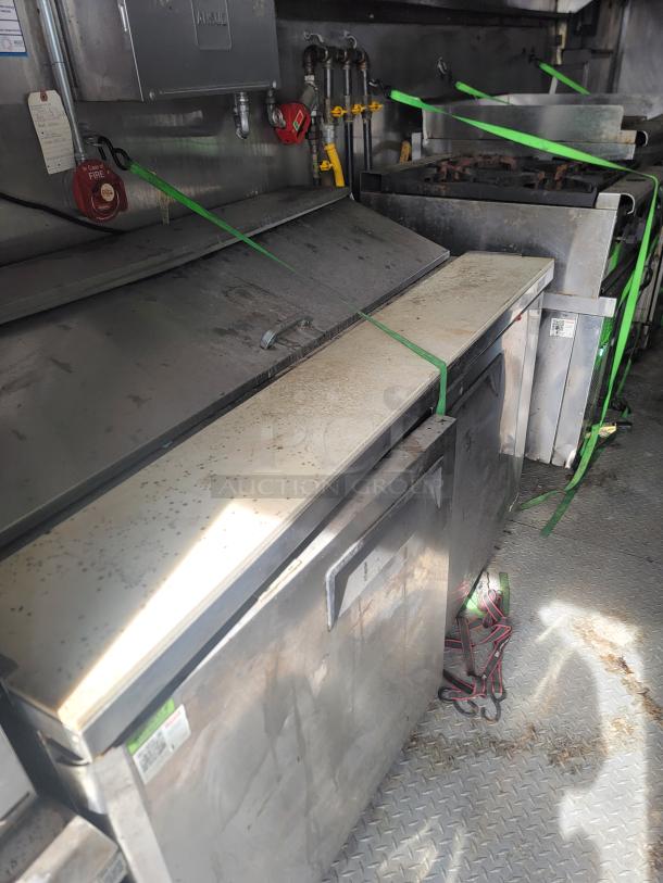 Commercial kitchen equipment setup, featuring industrial stoves and storage, secured with green straps, showing signs of use.