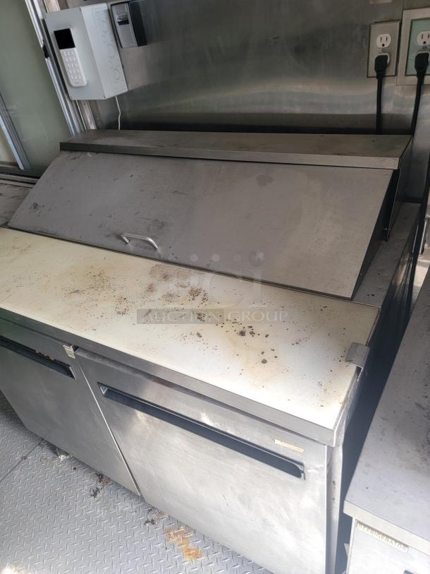 Stainless steel commercial refrigerated prep table with cutting board, showing signs of wear and stains, in used condition.