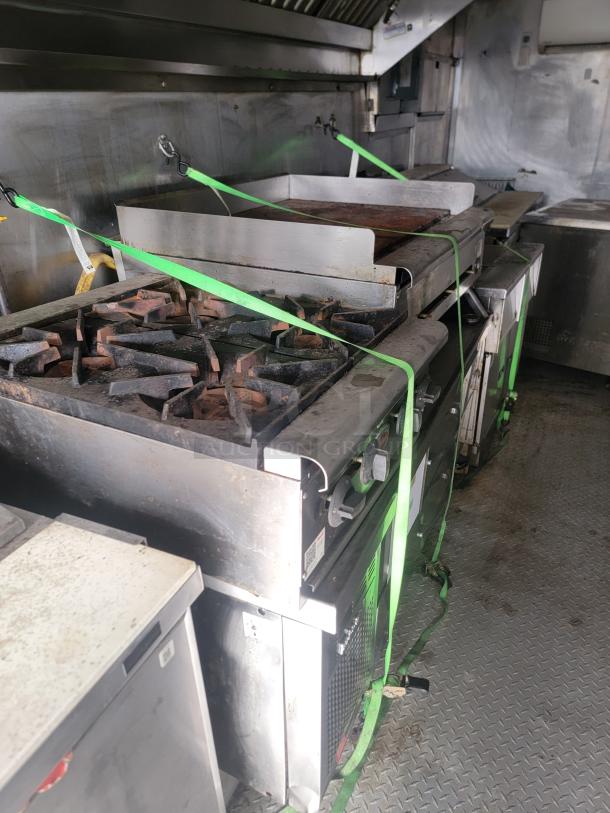 Commercial kitchen equipment featuring a gas stove and griddle, secured with green straps, in used condition.