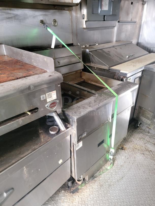 Commercial kitchen equipment including Pitco fryer, grill, secured with green strap, visible wear and grease residue.