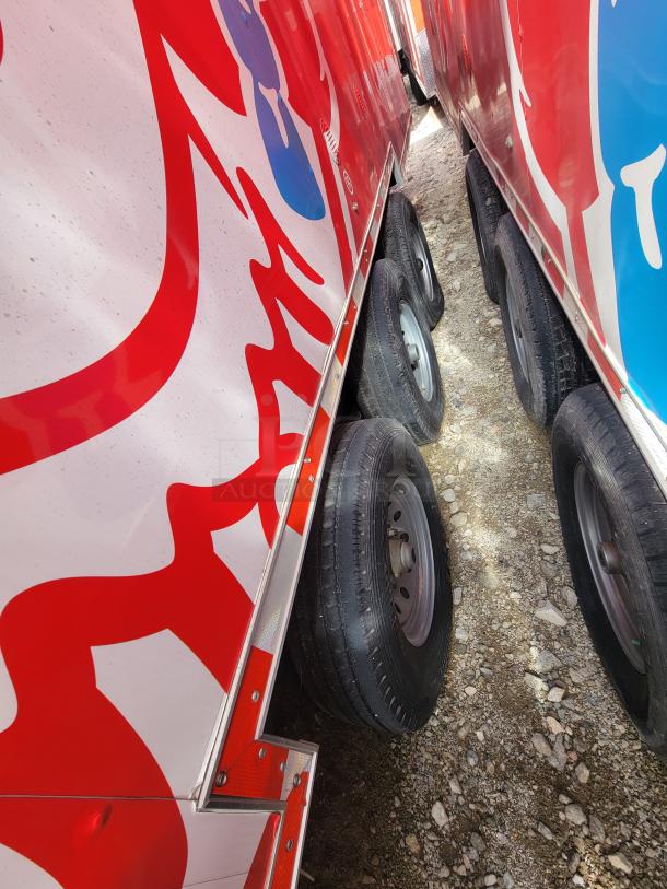 Row of red and blue trailers with visible wheels and vibrant graphics. Noticeable dirt and gravel ground. Some exterior wear.