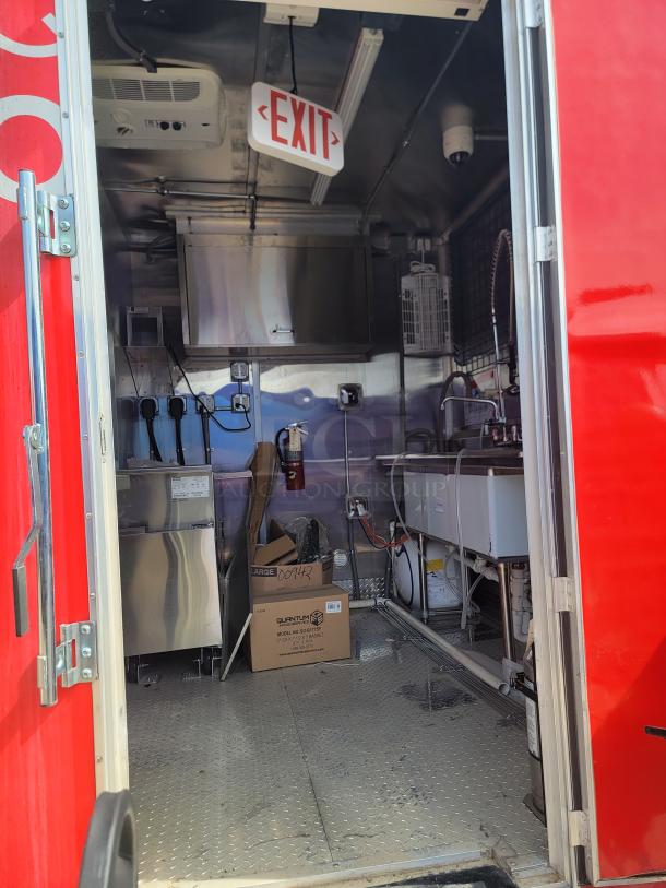 Mobile kitchen interior with stainless steel appliances, exit sign, and sink. Clean condition with visible wiring and storage boxes.