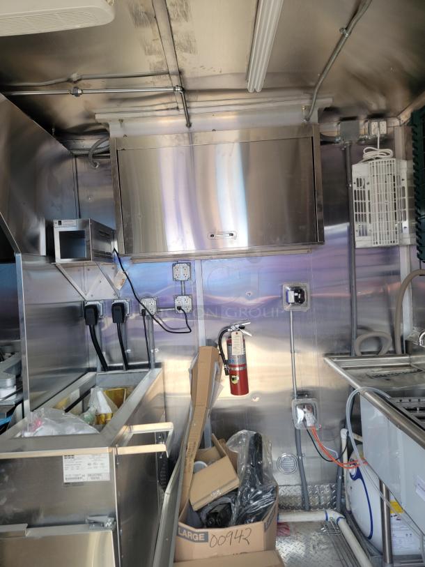 Industrial kitchen interior with stainless steel counters, storage cabinets, and utility outlets. Fire extinguisher visible.