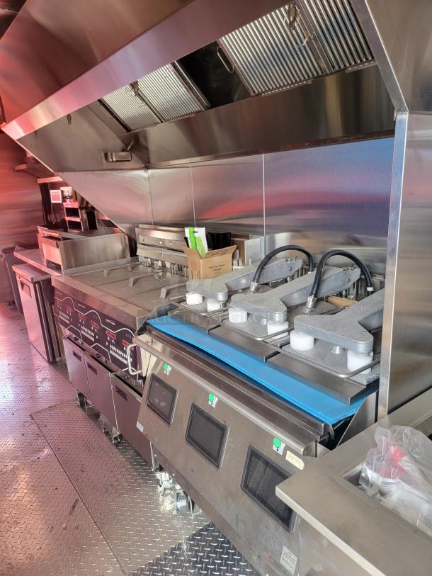 Commercial kitchen equipment with grills, fryers, and vent hoods in stainless steel. Pristine condition, ideal for restaurant use.