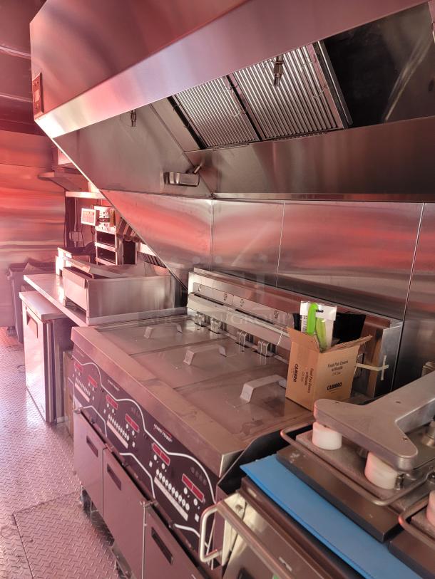 Commercial stainless steel kitchen equipment, including fryers and ventilation hood, in excellent condition. Safety markings visible.