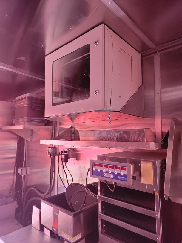Industrial kitchen equipment with stainless steel shelving and electrical components. Features include a control panel and metal storage bins.