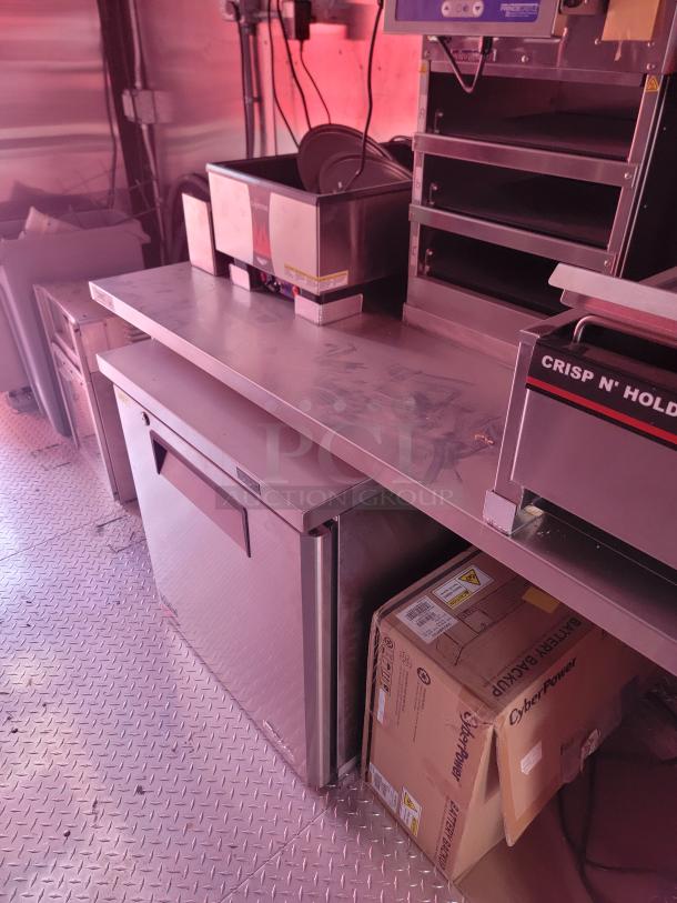 Commercial kitchen station with stainless steel countertop, Crisp N' Hold hot food station, and cooler. Box labeled CyberPower Battery Backup visible below.