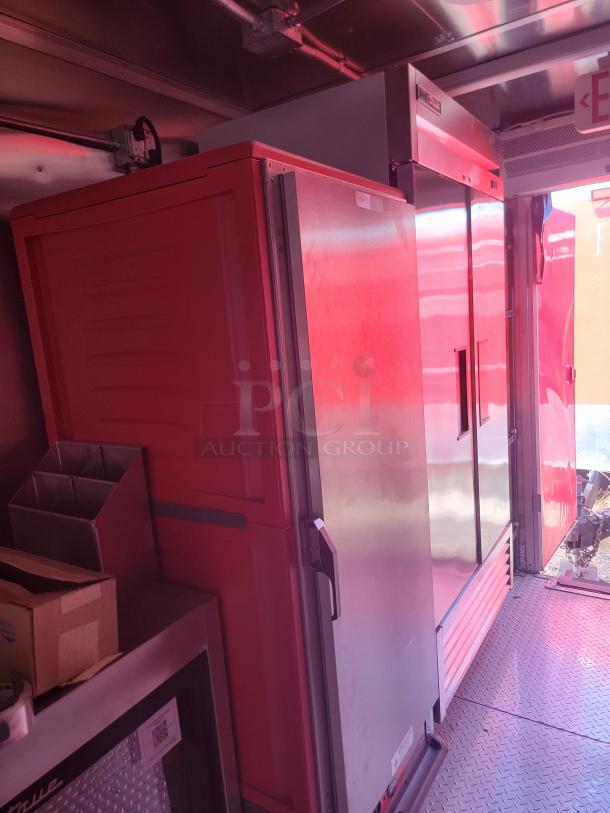 Industrial stainless steel refrigerator with dual doors, integrated into a commercial kitchen space.