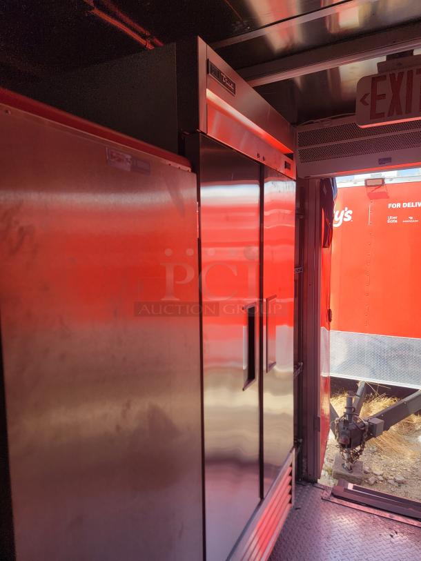 Commercial stainless steel refrigerator by True, dual doors, visible branding, good condition, located in a trailer.