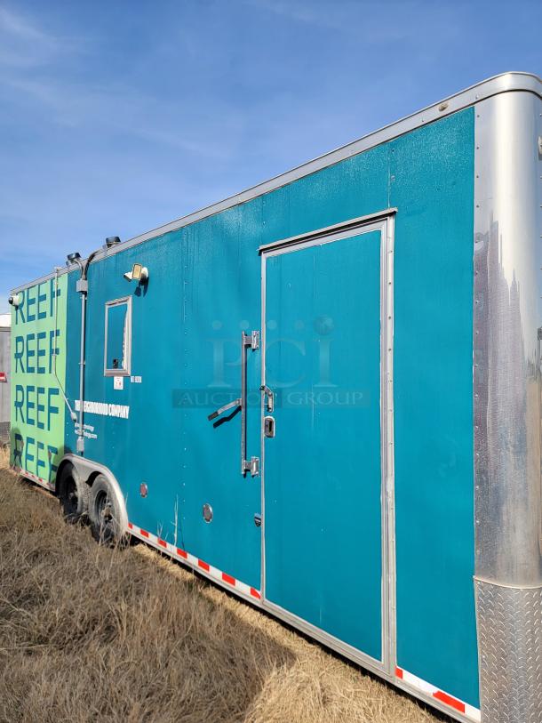 Blue mobile trailer with dual axles on grassy field. Marked "REFF" and "The Neighborhood Company." Visible wear and exterior lights.