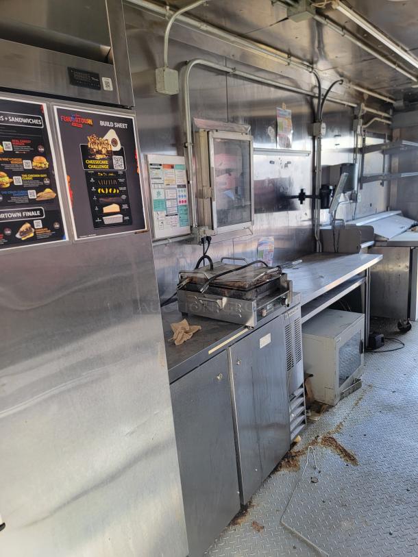Mobile food truck kitchen interior featuring stainless steel surfaces, grill, menu signs, and storage cabinets.