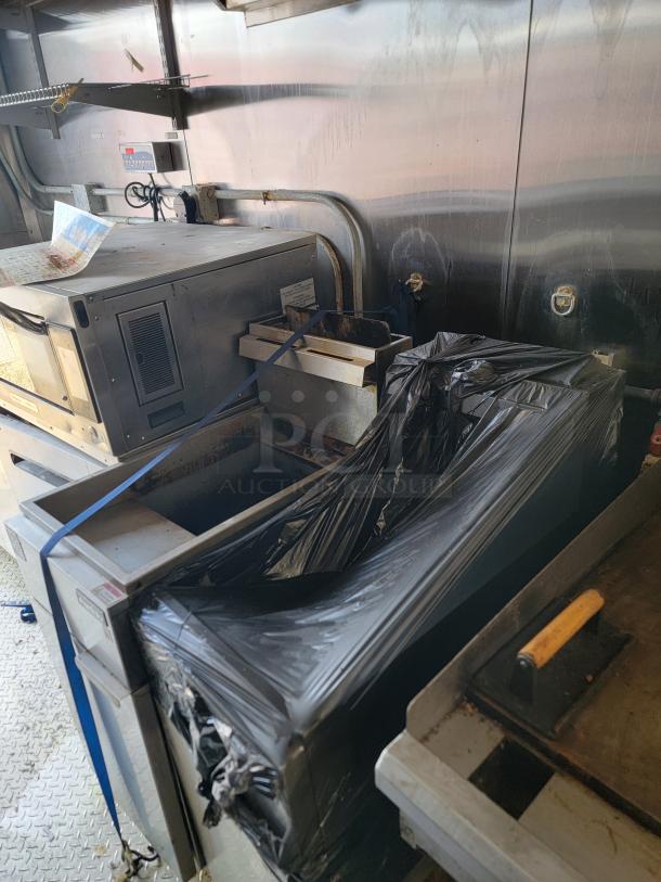 Commercial kitchen equipment with stainless steel surfaces and visible electronics, wrapped for protection.