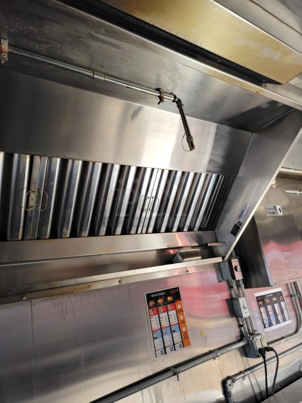 Commercial kitchen exhaust hood with ductwork, baffle filters, and an Ansul fire suppression system. Clean, stainless steel.