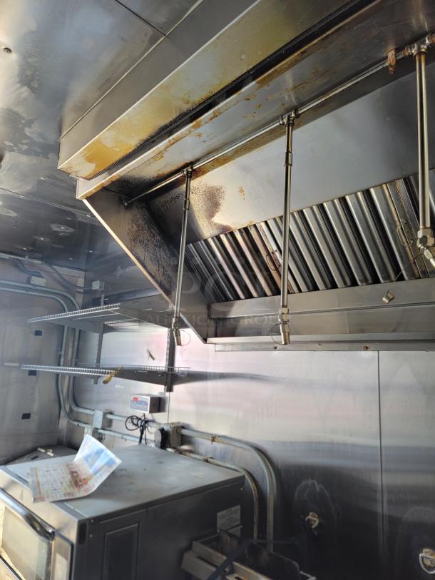Professional kitchen exhaust hood system with stainless steel construction, visible grease, and signs of use. Includes shelving and wiring.