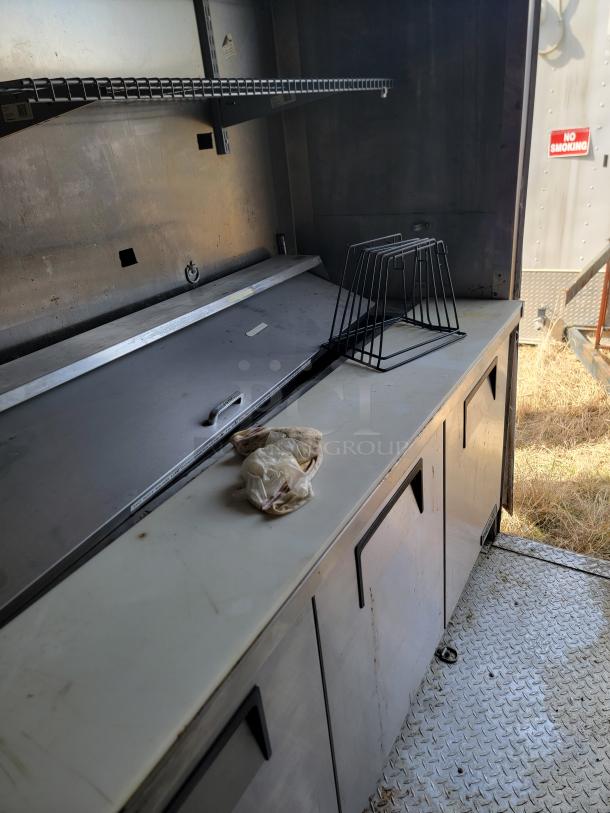 Metal workbench with storage cabinets, shelf, and wire rack. Appears well-used with some surface marks. "No Smoking" sign in background.