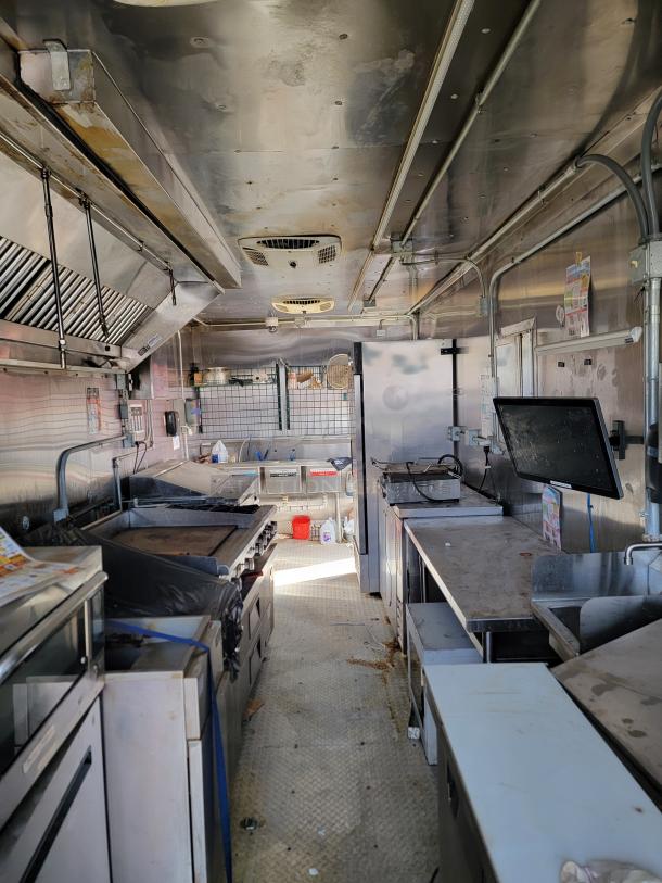 Commercial kitchen interior in a food truck, featuring stainless steel appliances, grill, sinks, and storage in used condition.