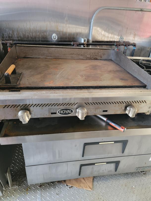 Royal commercial griddle with three knobs, used condition, visible wear on cooking surface, industrial kitchen setting.