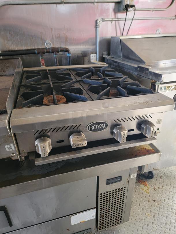 Royal commercial gas stove with four burners. Features stainless steel knobs, signs of use and rust, ideal for professional kitchens.