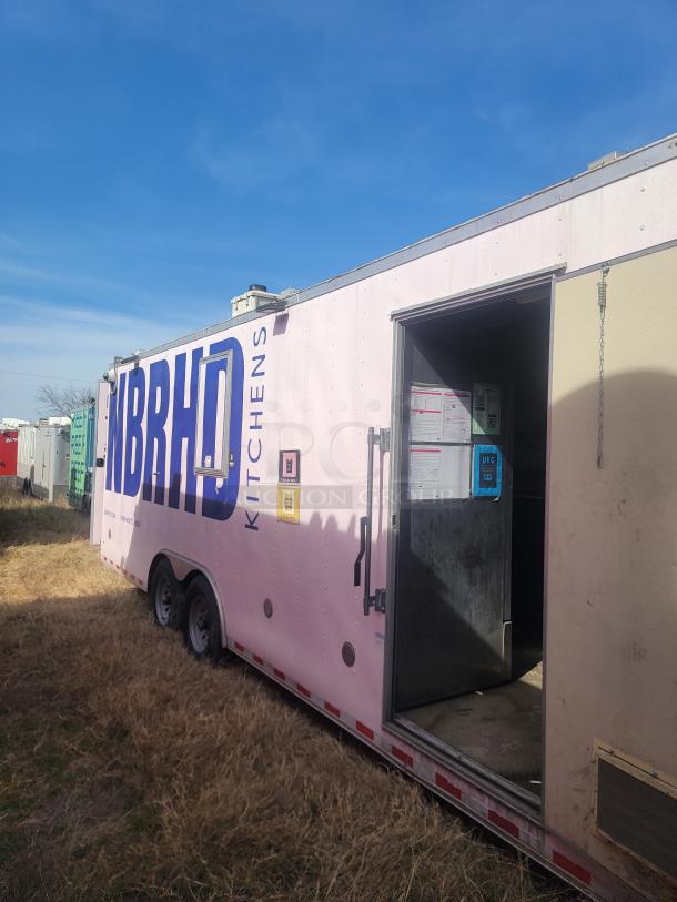 Mobile kitchen trailer with "NBRHD Kitchens" branding, light pink exterior, double axle, open door, located in grassy area.