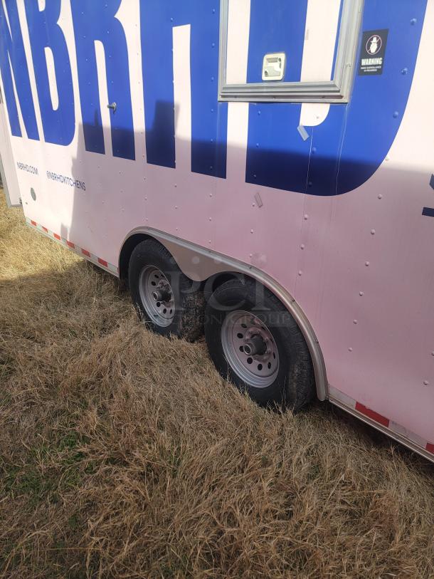 Utility trailer with dual axles, partially buried wheels, blue and pink exterior, visible branding "NBRHD," condition unclear.