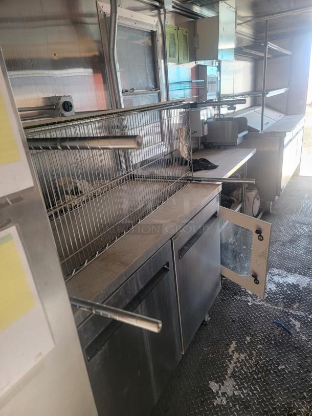 Commercial kitchen interior with stainless steel shelving, prep counters, and storage cabinets. Visible electrical outlet and notes posted.