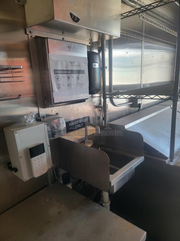 Stainless steel hand wash station with wall-mounted dispenser and instructional signage in a commercial kitchen.