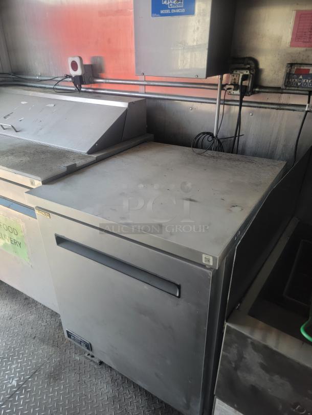 Stainless steel commercial freezer with sliding top, visible dents and marks, labeled "Freezer" with manufacturer tag.