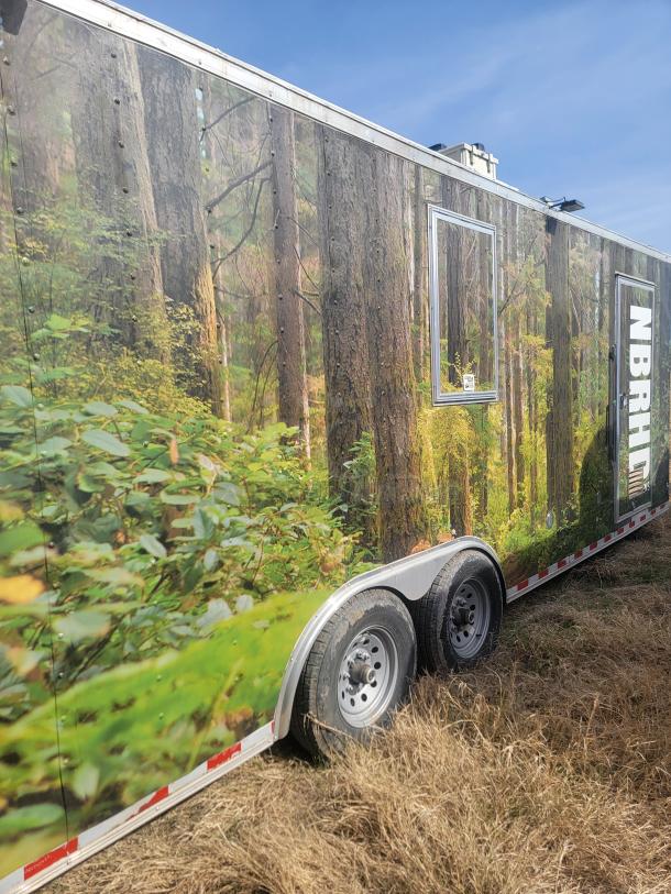 Large trailer with forest-themed exterior wrap, dual axles, window, and NBRH branding. Appears in good condition.