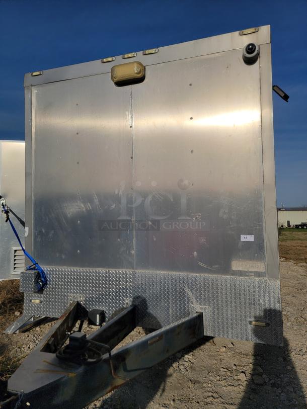 Aluminum trailer front view with treadplate base, visible camera, and lights. Slight wear, tag "Lexington" visible.