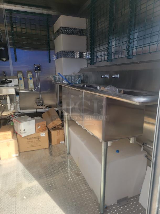 Commercial kitchen setup with stainless steel sinks, storage tanks, and pipes. Boxes labeled "Gurntum Model VO5-W2ATM160."