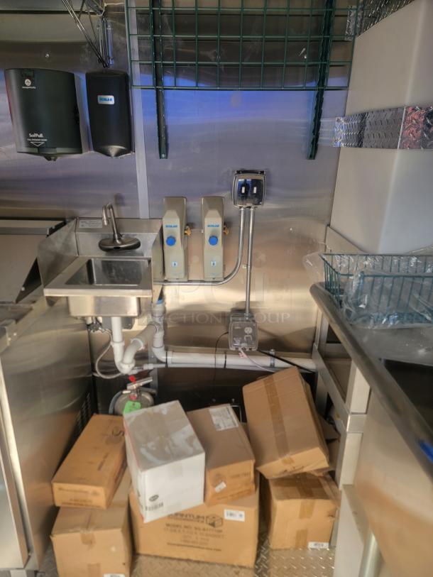 Commercial kitchen setup with wall-mounted soap dispensers, countertop sink, and stacked boxes. Clean condition.