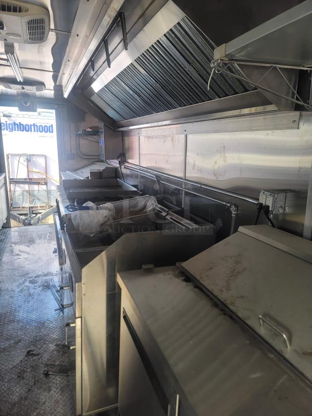Interior of a food truck featuring stainless steel kitchen equipment, including a ventilation hood and various cooking stations. Condition appears used.