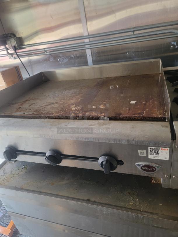 Wells countertop griddle with three knobs, used condition, metal exterior, visible wear, brand logo tag on front.